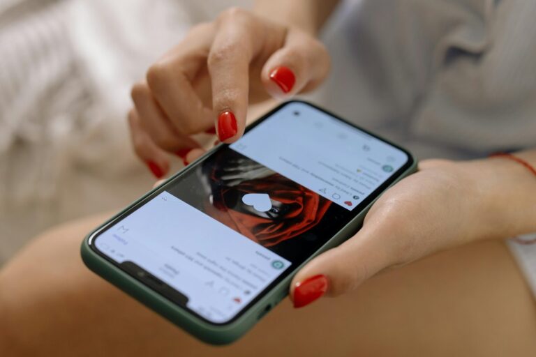 Dłonie z czerwonymi paznokciami przewijają ekran telefonu z serduszkiem na zdjęciu czerwonej róży